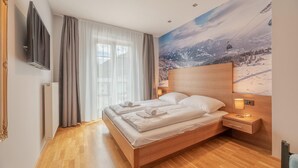 Une chambre d’hôtel avec un lit en bois, une télévision, une fresque murale représentant un paysage de montagne et une vue sur un télésiège.