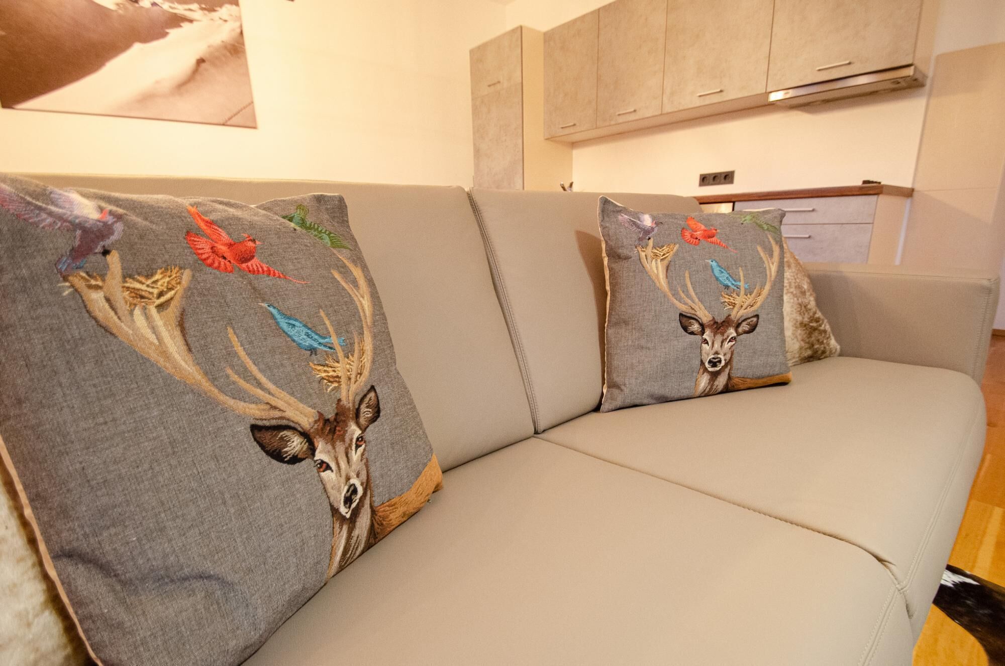 Ein beiges Sofa mit zwei dekorativen Kissen, verziert mit Stickereien von Hirschen und Vögeln.