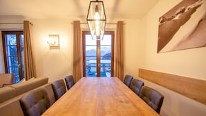 A dining area with a wooden table and leather chairs, a chandelier, and a view of mountains through a large window. - Post Residence Apartments 7B 150m From ski Lift (Zell am See)