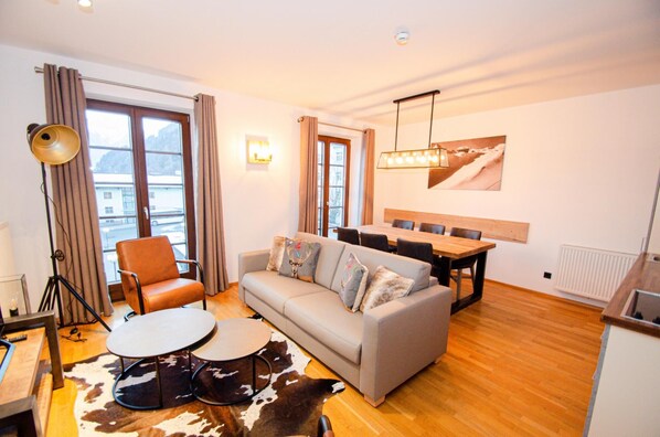 A modern living room with a sofa, two round tables, a dining table, and a cowhide rug. - Post Residence Apartments 7B 150m From ski Lift (Zell am See)