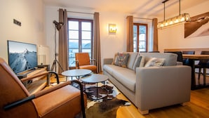 A modern living room with a sofa, a television, a lamp, and a dining area. - Post Residence Apartments 7B 150m From ski Lift (Zell am See)