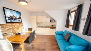 A modern living room with a blue sofa, wooden dining table, and a kitchen in the background. - Post Residence Apartments 10B Sauna Near ski lif (Zell am See)