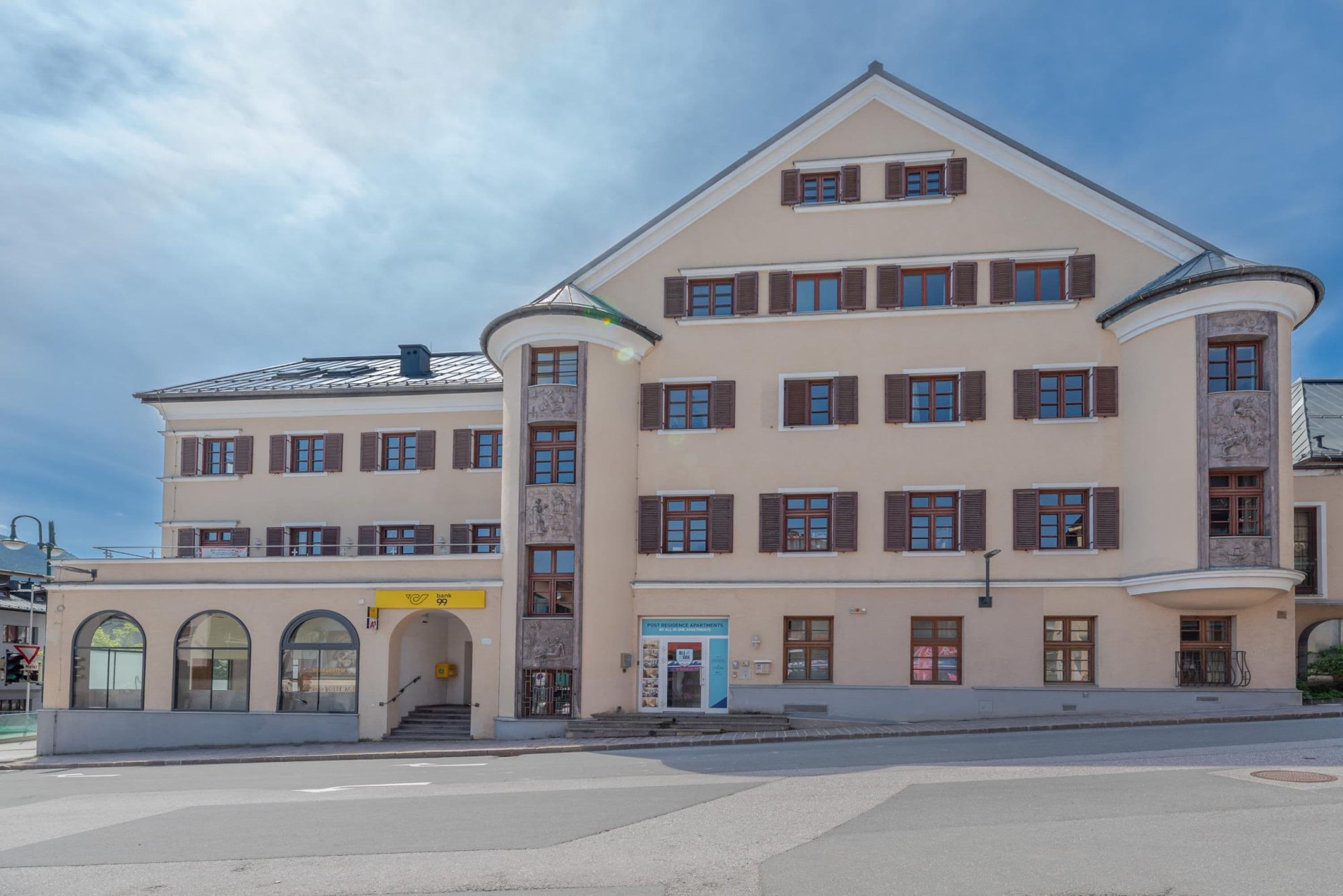A multi-story building with a central entrance, multiple windows, and a street in front.