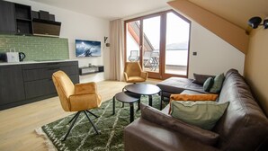 Eine moderne Wohnung mit Küche, einem Wohnbereich mit Sofa und Sesseln, einem kleinen runden Tisch und einem Balkon mit Blick.