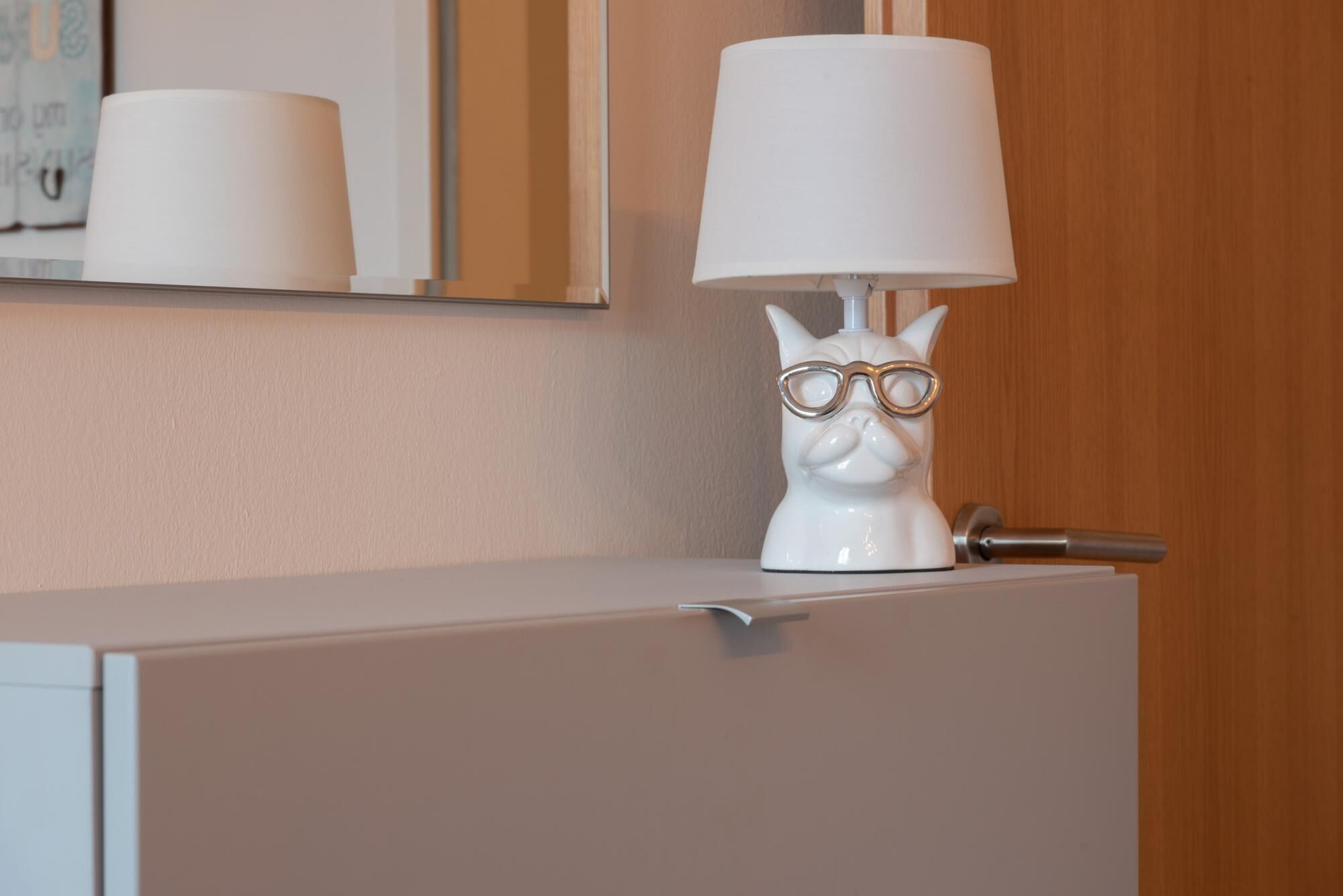 A white cat-shaped lamp with a white lampshade on a cabinet.