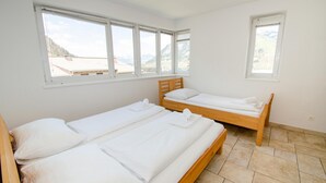 Een kamer met twee houten bedden, wit beddengoed en grote ramen met uitzicht op de bergen.