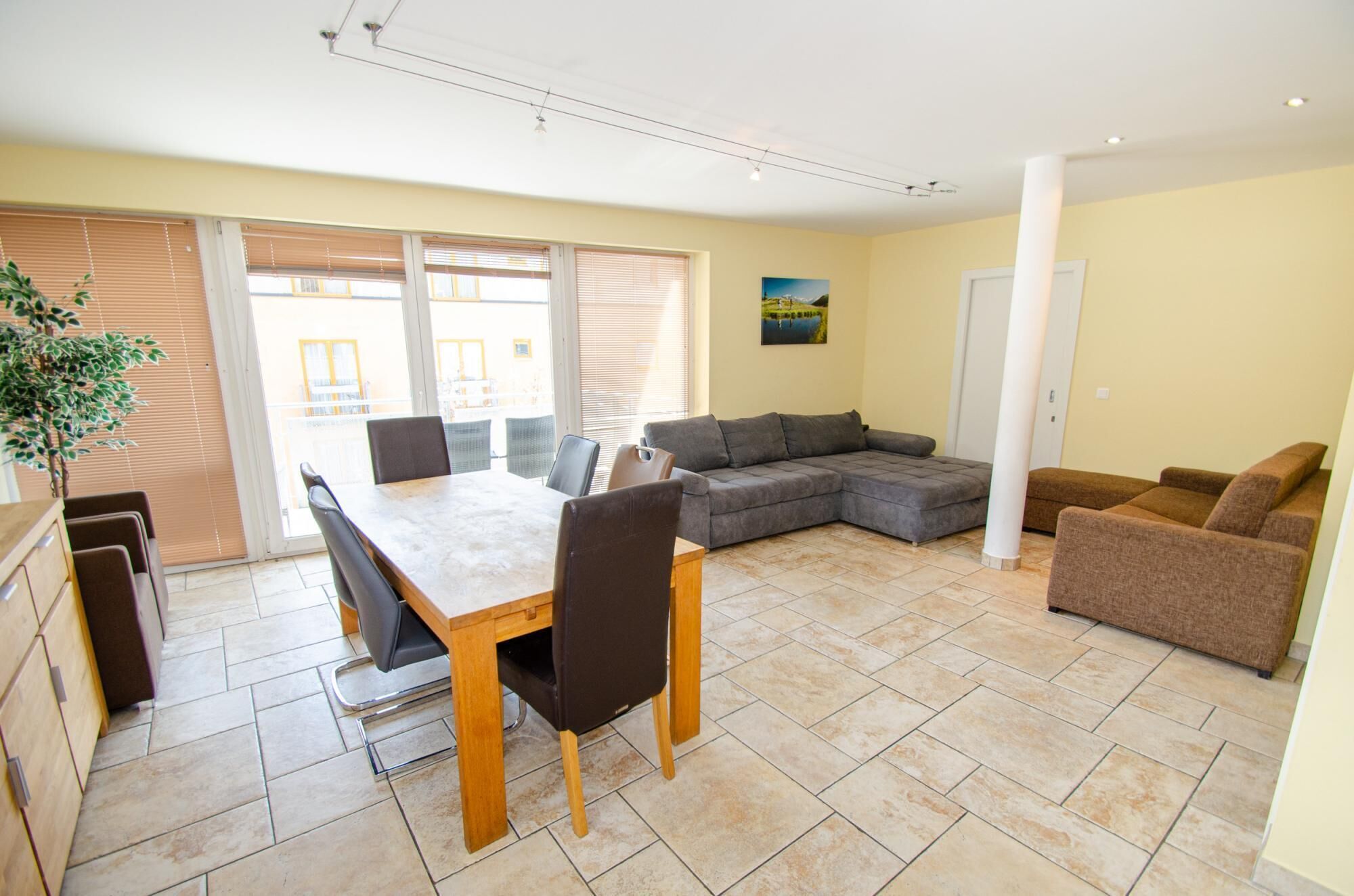 A spacious living area with a dining table, a gray sectional sofa, and a brown armchair.