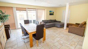 Een ruime woonkamer met een eettafel, een grijze hoekbank en een bruine fauteuil.