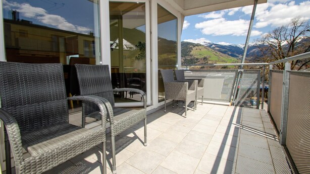 Een balkon met rieten stoelen en een tafel, met uitzicht op een bergachtig landschap.