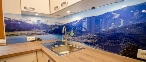 A modern kitchen with a wooden countertop, stainless steel sink, and a scenic mural of mountains and a lake.