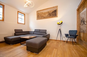 Un salon moderne avec un canapé d’angle, un petit pouf, une lampe sur pied et un tableau encadré accroché au mur.