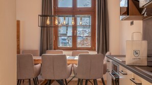 A modern kitchen with a dining area, featuring a wooden table, four chairs, and a hanging light fixture. - Post Residence Apartments 1C Sauna Near ski Lift (Zell am See)