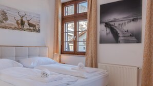 A hotel room with a large bed, a window with curtains, a radiator, and two paintings on the walls. - Post Residence Apartments 1C Sauna Near ski Lift (Zell am See)