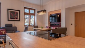 A modern kitchen with a central island, a dining area with a table and chairs, a sofa, and a TV mounted on the wall. - Post Residence Apartments 3C 150m From ski Lift (Zell am See)