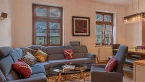 A living room with a grey sofa, a glass coffee table, and a view of snow-covered buildings through large windows. - Post Residence Apartments 3C 150m From ski Lift (Zell am See)