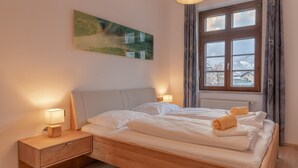 A bedroom with a wooden bed, two bedside tables with lamps, a window with curtains, and a painting on the wall. - Post Residence Apartments 3C 150m From ski Lift (Zell am See)