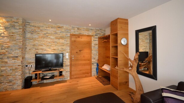 Una sala de estar moderna con pared de piedra, puerta de madera, mueble para televisor y un estante con forma de árbol.