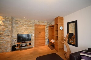 Een moderne woonkamer met een stenen muur, een houten deur, een tv-meubel en een bijzondere plank in de vorm van een boom.