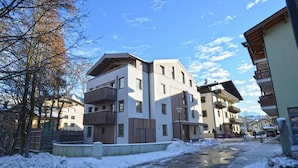 Un edificio de varios pisos con balcones, suelo cubierto de nieve y cielo despejado.