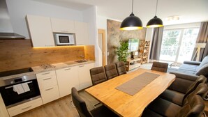 Una cocina moderna con microondas integrado, un comedor con mesa de madera y sillas de cuero, y una sala de estar con sofá y planta.