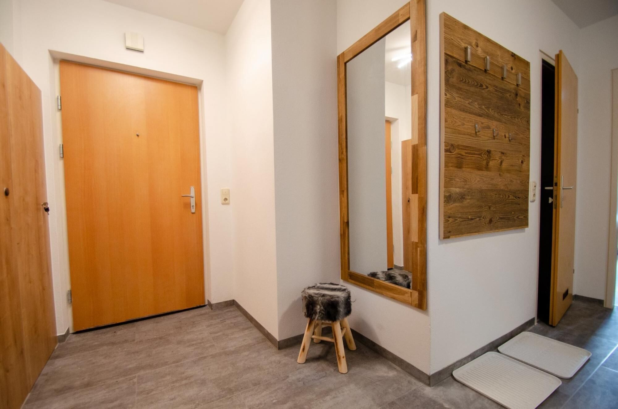 Ein Flur mit Holztüren, einem großen Spiegel und einem kleinen Hocker.