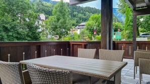 An outdoor seating area with wicker chairs and a table, overlooking a forested hillside.