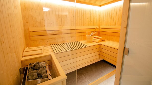 A sauna with wooden walls and benches, a bench with a towel, and a container of stones.