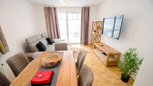 A modern living room with a wooden dining table, grey sofa, and a TV mounted on the wall. - Apartment Summer Winter Fun II - 200 m From ski (Zell am See)