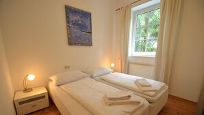 Un dormitorio con dos camas, una mesita de noche, una lámpara y una ventana con cortinas.