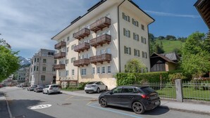 Un edificio de varios pisos con balcones, coches estacionados y una vista despejada de un paisaje montañoso.