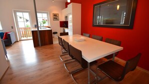 Una cocina moderna con armarios blancos, una isla de madera y un comedor con una mesa blanca y sillas de metal.