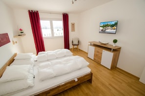 Quarto de hotel com uma cama grande, uma escrivaninha de madeira, um frigorífico pequeno e uma televisão na parede.