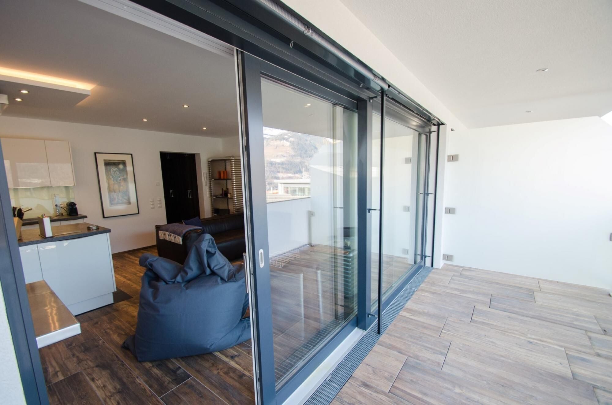 A modern interior with a kitchen, seating area, and large glass doors leading to a balcony.