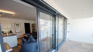 A modern interior with a kitchen, seating area, and large glass doors leading to a balcony. - Superb Alpine Lodges Zell am See 6-8pax (Zell am See)