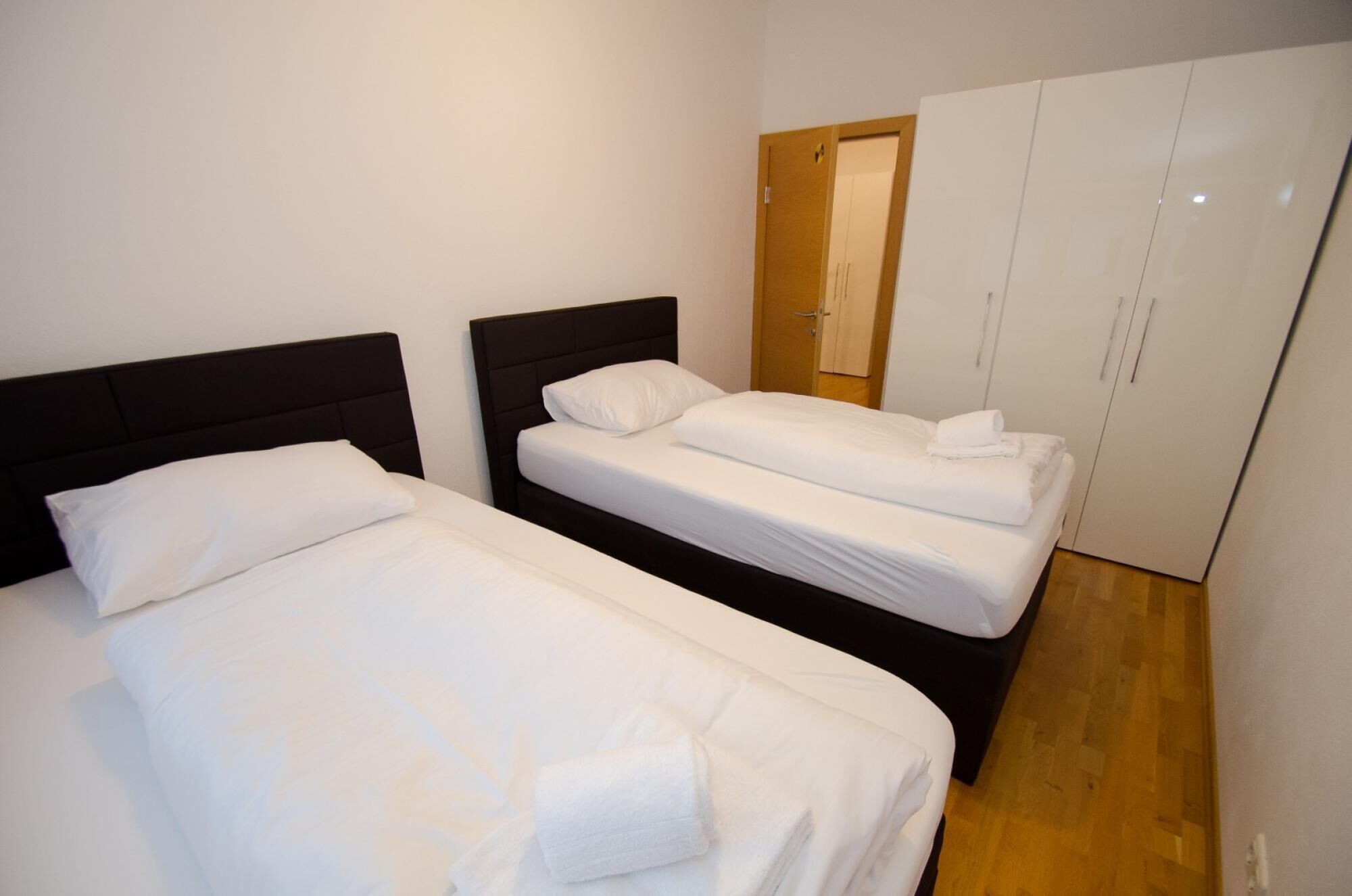 Ett hotellrum med två separata sängar, en garderob och ett trägolv.