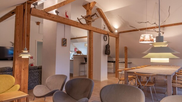 Un vaste espace de vie agrémenté de poutres en bois, de meubles modernes et d’un coin repas avec une grande table et des chaises.