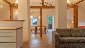 Un intérieur moderne avec des poutres en bois, un coin repas avec une table et des chaises en bois, et un canapé gris.
