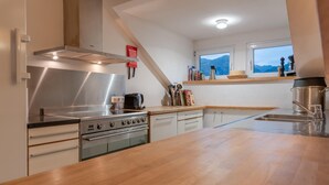 Une cuisine moderne dotée d’appareils électroménagers en acier inoxydable, de plans de travail en bois et offrant une vue sur les montagnes par la fenêtre.
