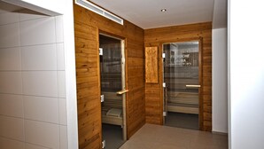 Ein Flur mit Holzwänden und Fliesenboden, der zu einem Saunaraum mit Glastür und Temperaturanzeige führt.