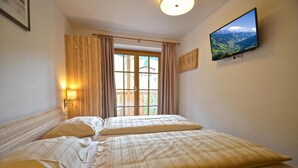 Ein Hotelzimmer mit zwei Betten, einem großen Fenster mit Vorhängen, einem an der Wand montierten Fernseher und einem Holz-Kopfteil.
