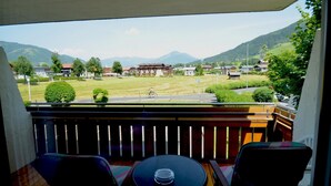 A balcony with a view of a mountain landscape, a cyclist on the road, and a building in the distance. - Deluxe Studio Kaprun TOP 12 (Kaprun)