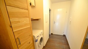 A laundry room with a washing machine, wooden cabinets, and a tiled floor. - Deluxe Studio Kaprun TOP 12 (Kaprun)
