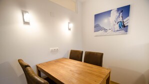 A dining area with a wooden table and four brown chairs. There is a wall-mounted light fixture and a painting of a skier on the wall. - Deluxe Studio Kaprun TOP 23 (Kaprun)