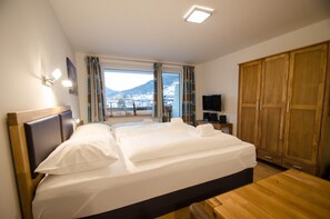 Ett hotellrum med en stor säng, en TV, en garderob och ett fönster med utsikt över en stad och berg.
