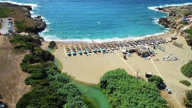 Vista aérea de una playa con un área de estacionamiento, una fila de sombrillas y un pequeño edificio.