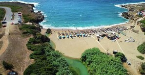 Vista aérea de una playa con un área de estacionamiento, una fila de sombrillas y un pequeño edificio.