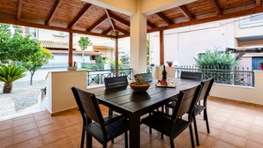 Un patio cubierto con una mesa y sillas de madera, plantas en macetas y vistas de los edificios circundantes.