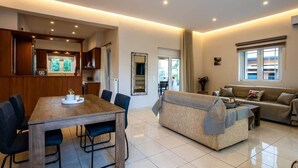 Una sala de estar moderna con una mesa de comedor de madera, sillas azules, un sofá color beige y un ventanal con cortinas.