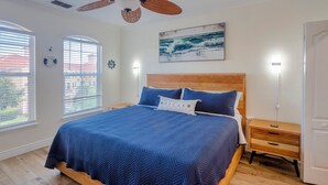 A bedroom with a wooden bed, a blue bedspread, a nightstand, and a wall-mounted artwork.