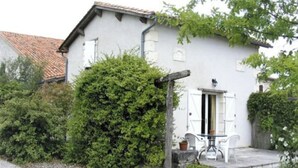 A white building with a tiled roof, a gravel driveway, and a small patio with a table and chairs. - 1 Bedroom Private vacation home in Ronsenac (Ronsenac)